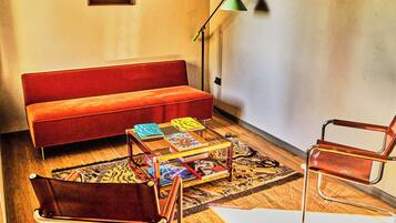Ein Wohnzimmer mit einem roten Sofa, einem Couchtisch mit Büchern, einer Stehlampe und einem modernen Sessel.