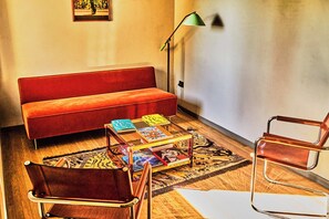 Un salon avec un canapé rouge, une table basse sur laquelle sont posés des livres, un lampadaire et un fauteuil moderne.
