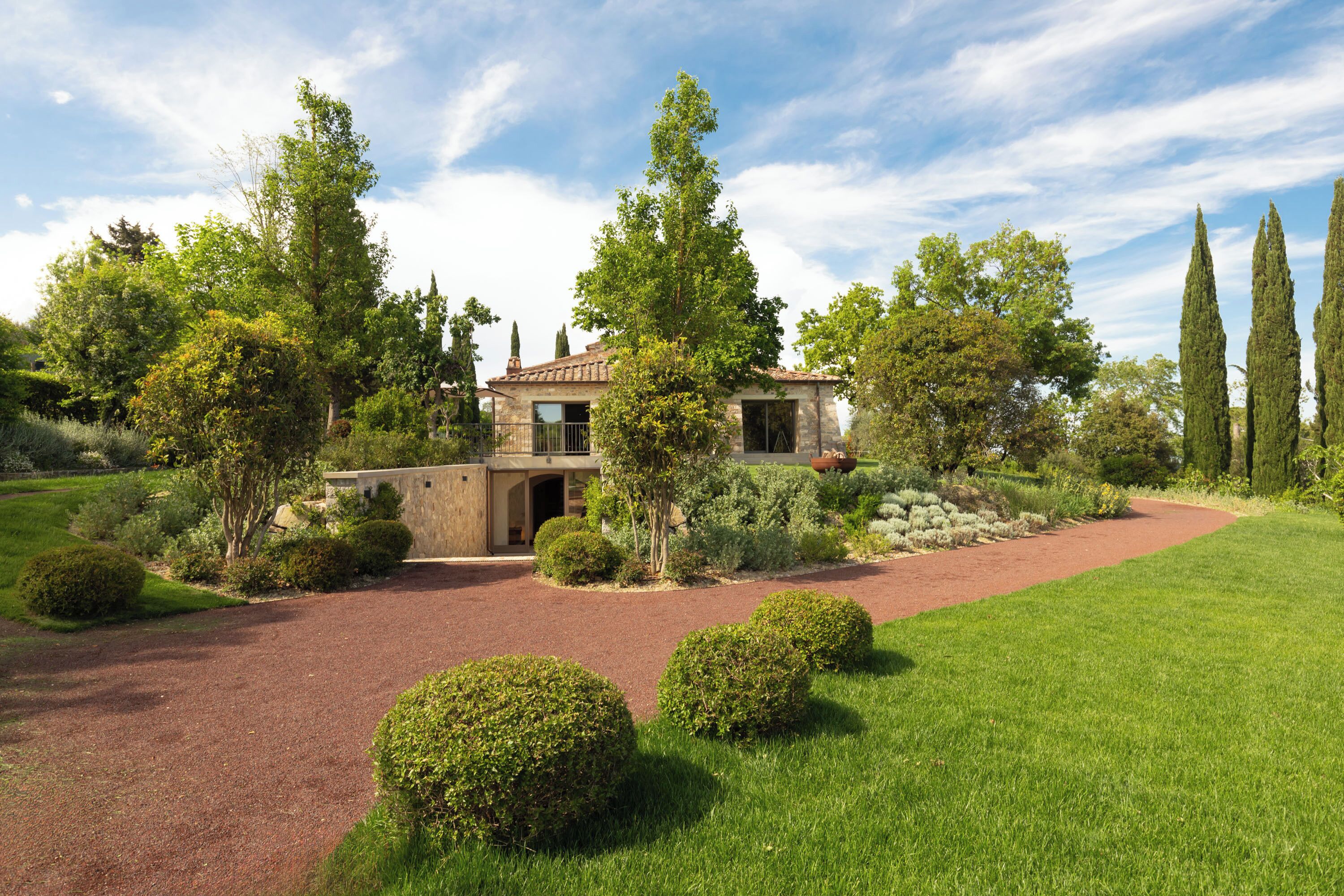 A house with a paved driveway, surrounded by well-maintained lawns and trees.