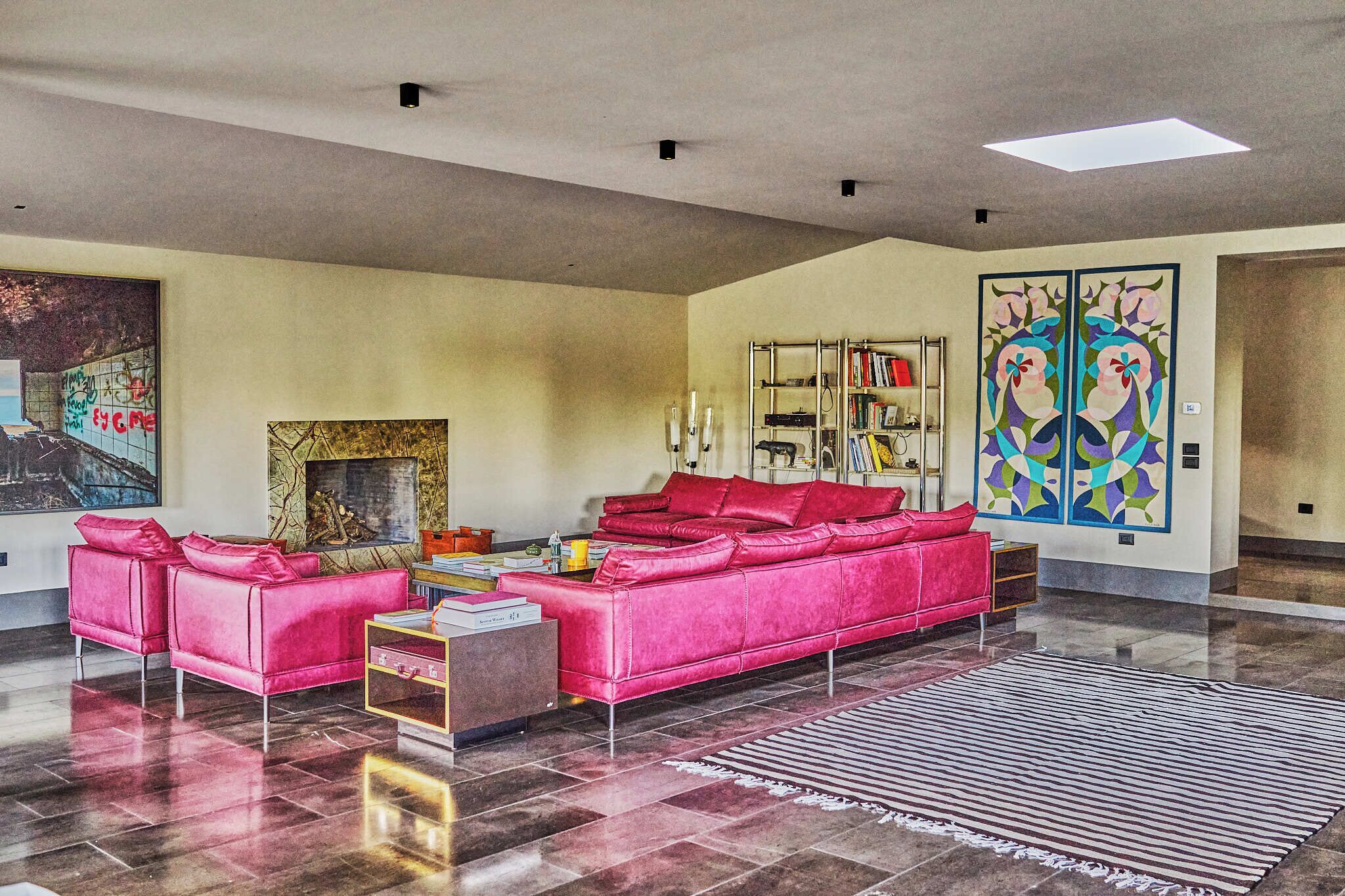 A spacious living room with a red sofa set, a fireplace, and a large abstract painting.