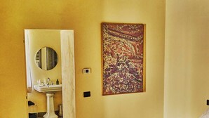 A bedroom with a bed, a wooden floor, a bathroom with a sink and mirror, and a painting on the wall. - Godiluva, wine villa (Toscana)