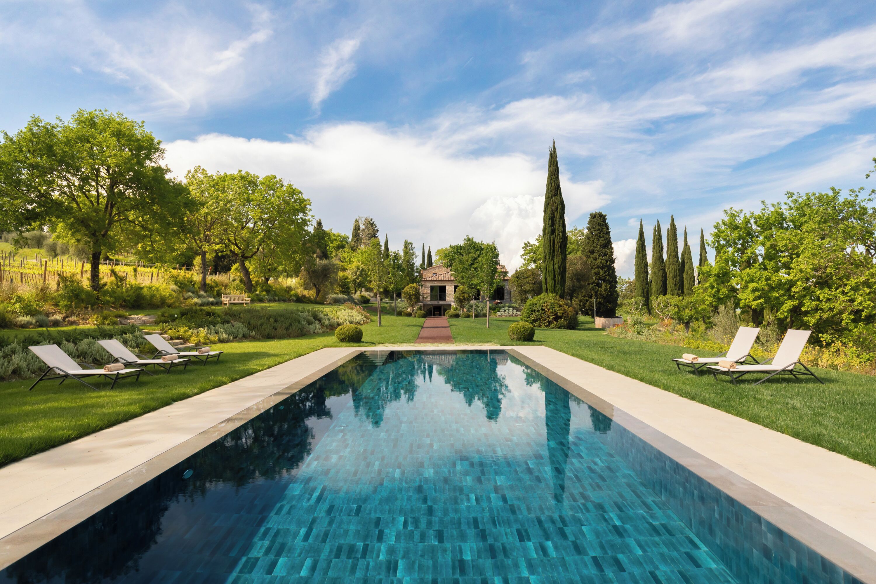 A rectangular swimming pool with clear blue water, surrounded by a well-maintained lawn and trees.