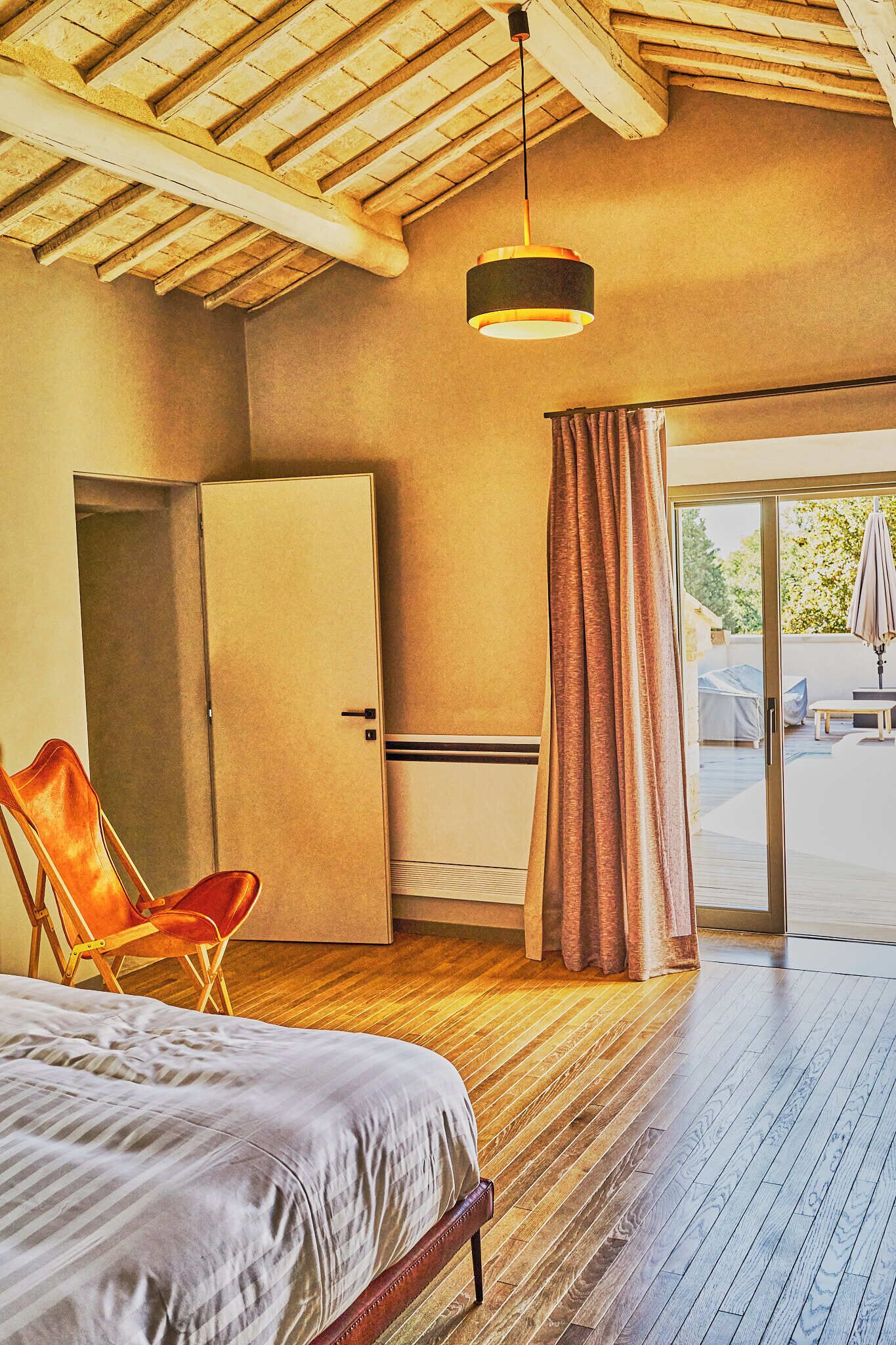 Ein Zimmer mit einem Bett, einem Sessel, einem Kleiderschrank und einer Glastür, die zu einem Außenbereich führt.