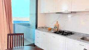 A modern kitchen with white cabinets, a marble countertop, a gas stove, and a view through a glass door.
