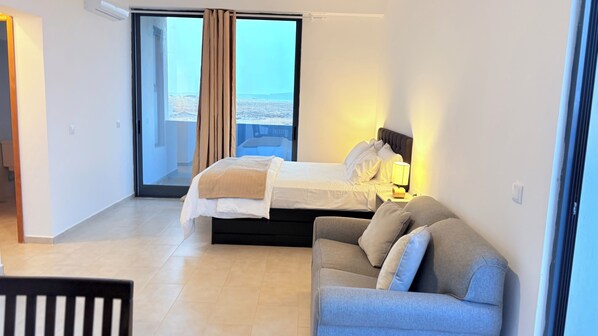 A hotel room with a bed, a sofa, a nightstand, and a view through a glass door.