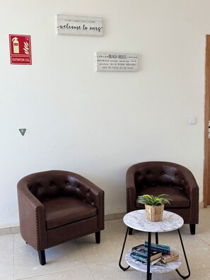 Two brown leather armchairs, a small round table with a plant and books, and two signs on the wall: one welcoming guests and another with beach rules. - JoLi Beach House - Second Floor T1 Beautiful and Authentic Island Living (Santa Maria)