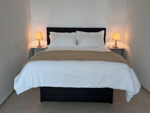 A neatly made bed with white bedding and a brown throw, flanked by two bedside tables with lamps.