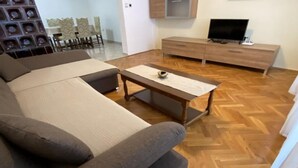 Un soggiorno con divano, tavolino, televisore e pavimento in legno a spina di pesce.