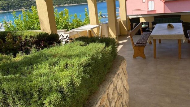 Zona relax esterna coperta con tavolo e sedie, affacciata su uno specchio d'acqua e un edificio rosa.