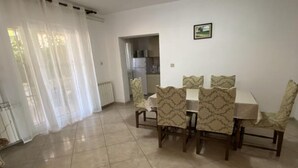 Zona pranzo con tavolo e sedie, cucina sullo sfondo e una finestra con tende leggere.