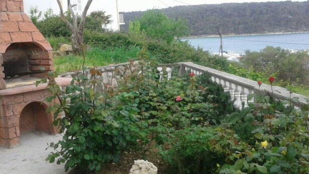 Un horno de ladrillo al aire libre, una casa blanca y una vista de un lago con colinas al fondo.