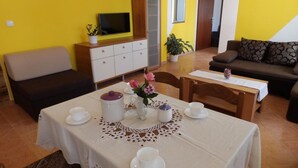 Un comedor con una mesa dispuesta para dos, un mueble con televisor y un sofá en una habitación de paredes amarillas.