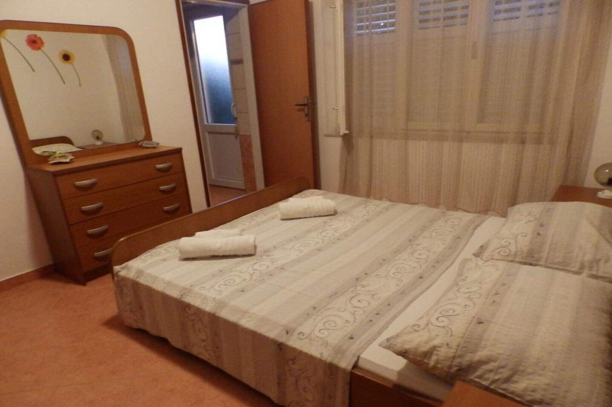 A bedroom with a bed, a wooden dresser with drawers, a mirror, and a window with curtains.