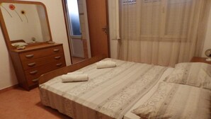 Un dormitorio con cama, cómoda de madera con cajones, espejo y ventana con cortinas.