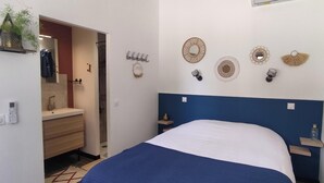 A bedroom with a bed, a bedside table, a wall-mounted mirror, and a small shelf with a plant. - Gite Casa Tutel (Esperce)