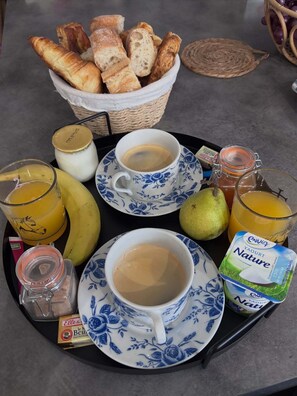 Ein Frühstücksbrett mit Croissants, Kaffee, Saft, einer Birne, einer Banane und einem Becher Envia Nature Joghurt.