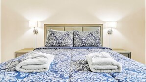 A neatly made bed with patterned bedding, two bedside lamps, and folded towels on the bed. - TruStay in Central CT (Manchester)