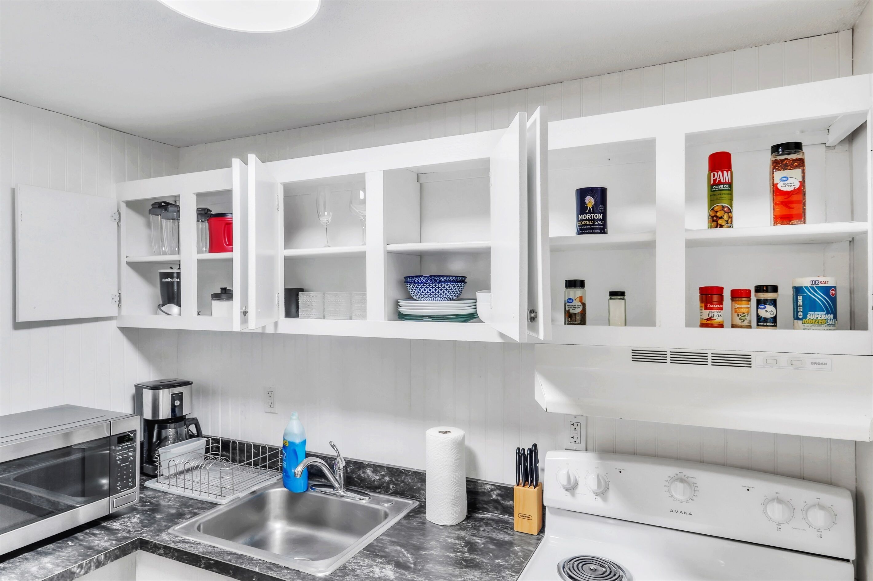 Een moderne keuken met een inbouwmagnetron, koffiezetapparaat, spoelbak en een fornuis.