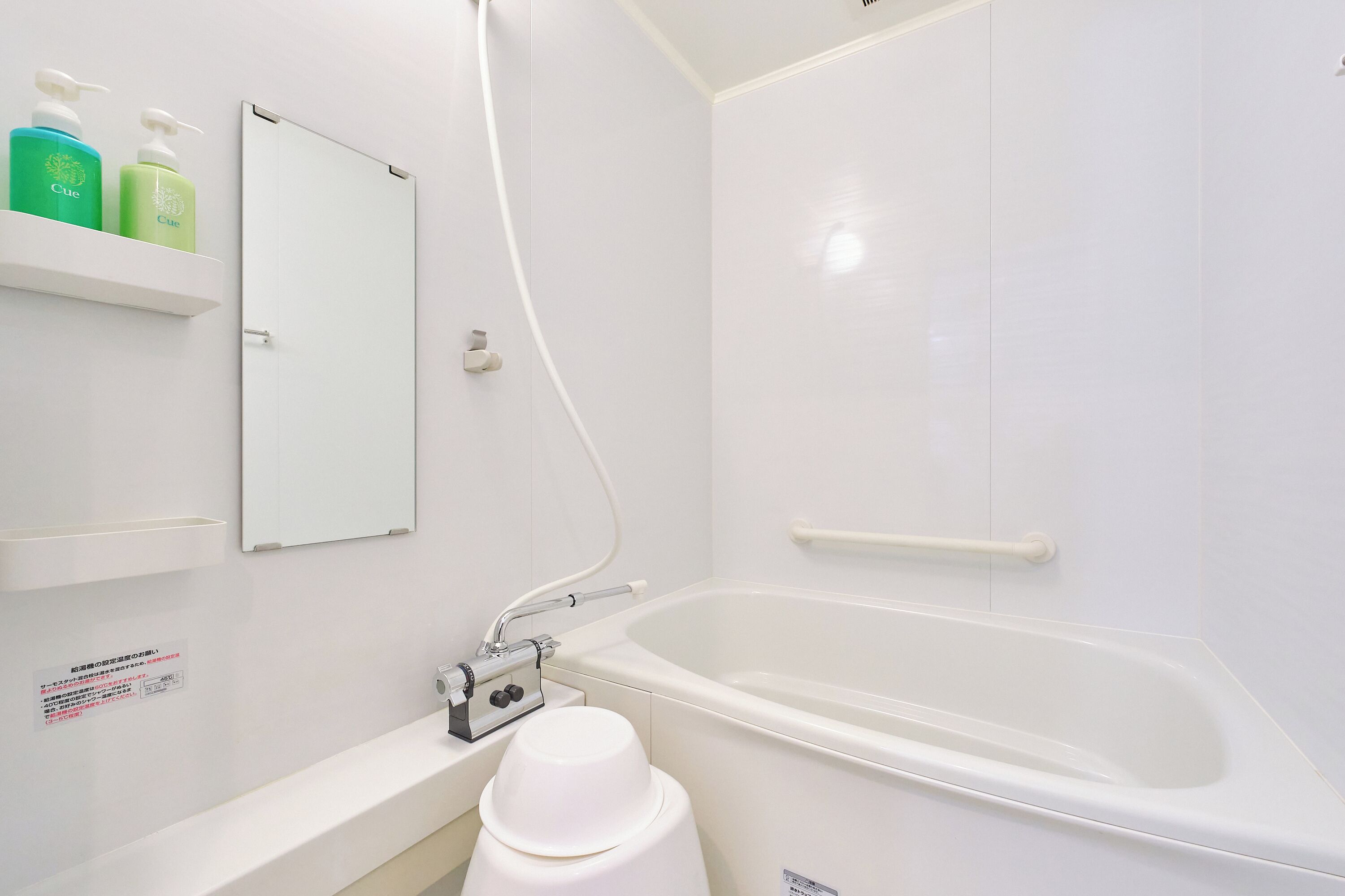 A modern bathroom with a bathtub, a shower, and a toilet. There are two bottles of lotion on a shelf.