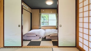 Ein traditioneller japanischer Raum mit Tatami-Boden, Futonbett, Schiebetüren und Blick auf Grünfläche.