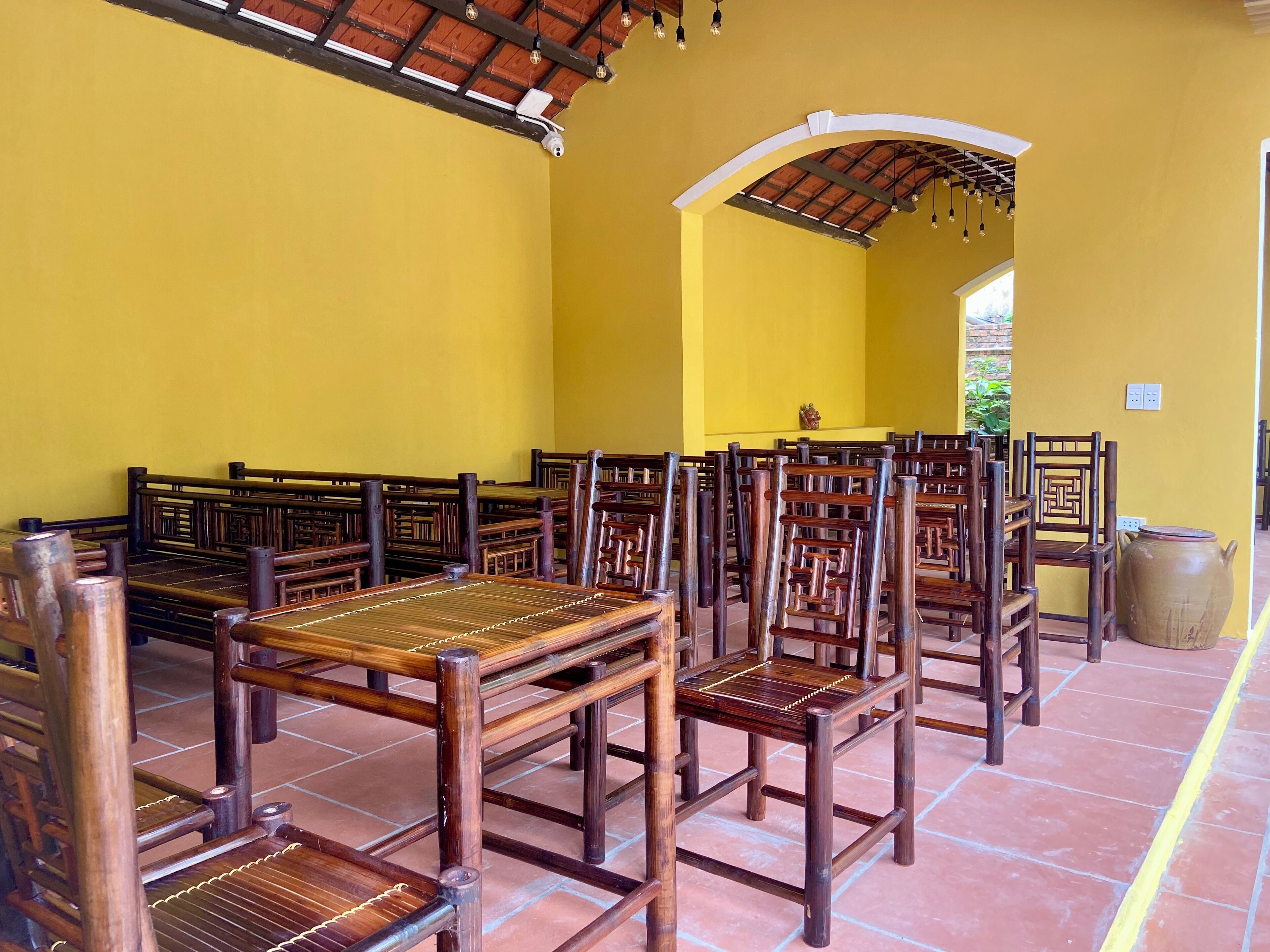 A room with wooden benches and chairs arranged in rows, a tiled floor, and a yellow wall.