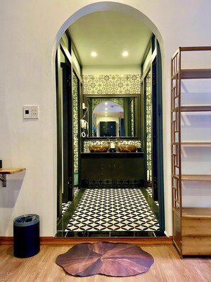 A hallway leading to a bathroom with patterned tiles, a mirror, and a vanity with a sink and towel rack. - Ann Garden Retreat Cat Ba (Hai Phong)