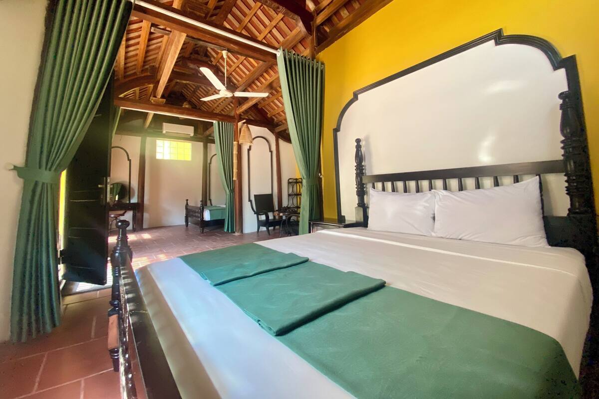 Ein Schlafzimmer mit Himmelbett, grünen Vorhängen und einer Holzbalkendecke.