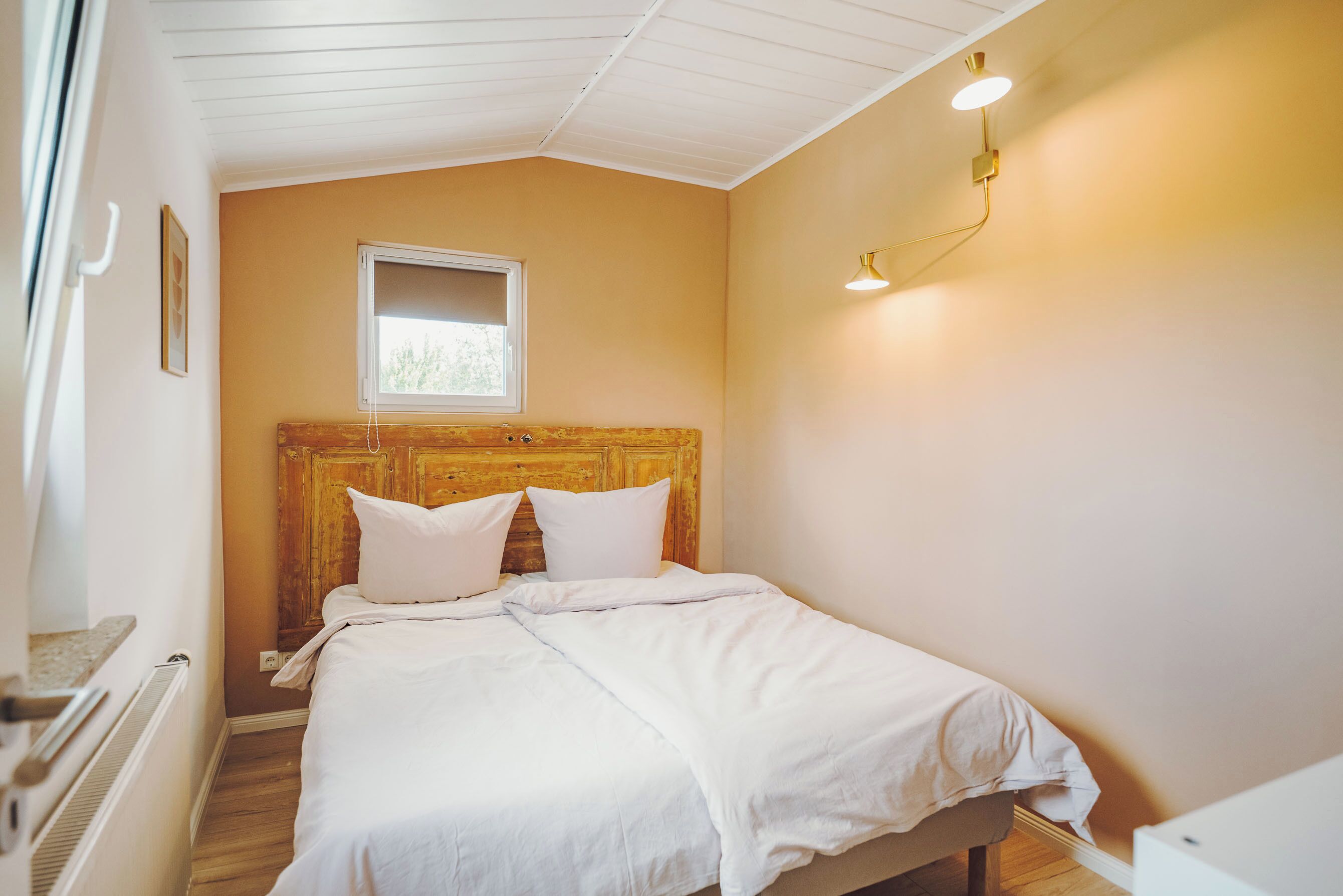Een slaapkamer met een houten hoofdbord, een raam en een bedlampje.