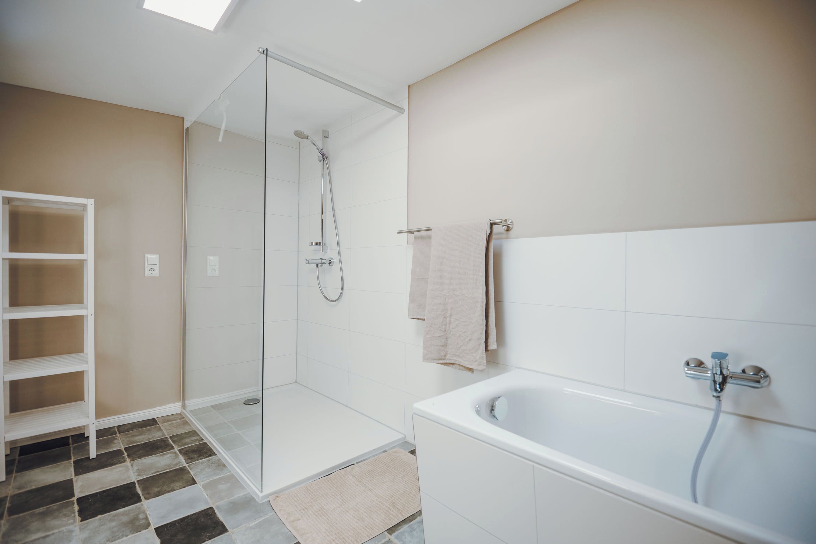 A modern bathroom with a glass-enclosed shower, a white bathtub, and a built-in shelf.
