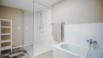 A modern bathroom with a glass-enclosed shower, a white bathtub, and a built-in shelf.
