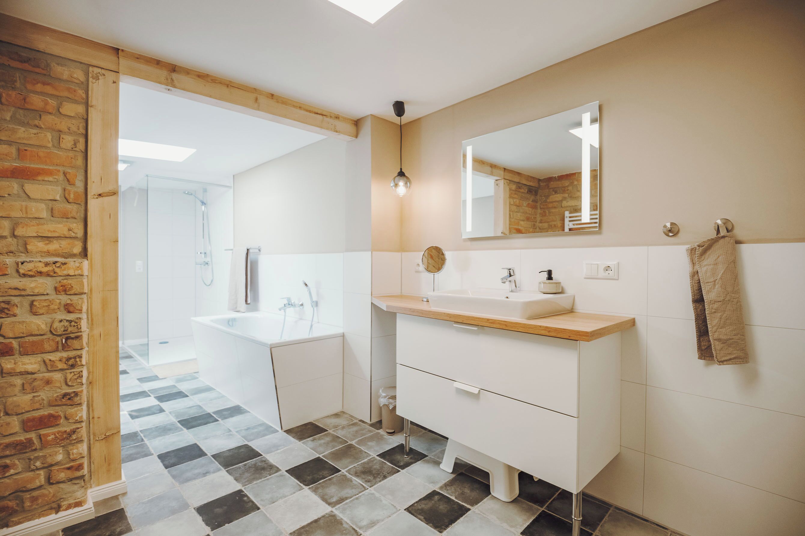 A modern bathroom with a wooden-framed glass door leading to a shower area, a white sink with a wooden countertop, and a mirror above the sink.