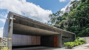 A modern building with a concrete exterior, a large open entrance, and a wooden door. - Stunning Views -  Villa Maan Ingfah VMI1 (Chalong)