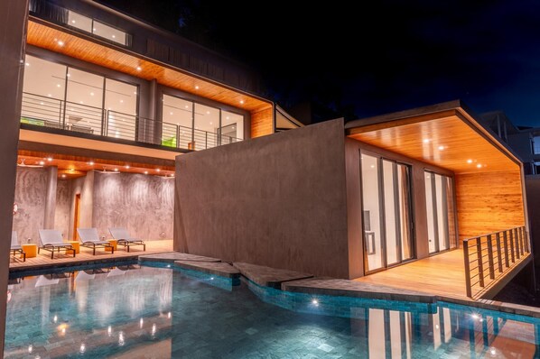 Una casa moderna con piscina, ampie finestre e un terrazzo in legno.