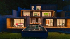 Una moderna casa a più piani con piscina al centro, ampie finestre in vetro e un prato curato.