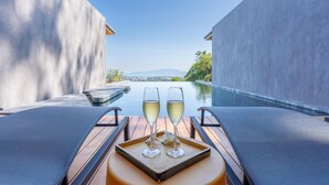 A terrace with two lounge chairs, a tray with two glasses of white wine, and a view of a body of water and distant landscape. - Stunning Views -  Villa Maan Ingfah VMI1 (Chalong)