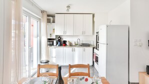 Eine helle Küche mit weißen Schränken, einem Esstisch mit Stühlen und einem Kühlschrank.