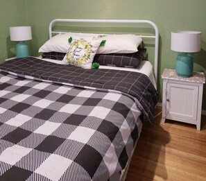 Een bed met een zwart-wit geruite sprei, twee kussens met bloemmotieven en een wit metalen hoofdbord.