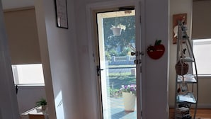 Een gang met een houten vloer die leidt naar een deur met uitzicht op een tuin en een balkon.