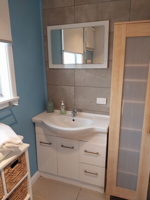 Een badkamer met een witte wasbak, een spiegel erboven en een houten kastje met een glazen deur.