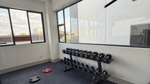 A gym with weightlifting equipment, a bench, and a large window with a view of buildings.