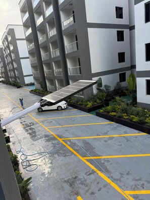 A modern multi-story residential building with balconies, a parking area with yellow lines, and a solar panel.