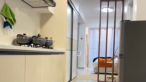 Una cocina moderna con estufa a gas, ollas y un refrigerador. Hay un pasillo que conduce a una sala de estar con sofá y ventana.