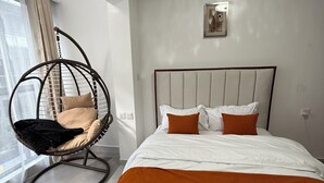 A modern bedroom with a large bed, a hanging chair, and a city view.