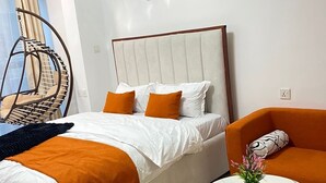 Una habitación de hotel moderna con una cama grande, un sillón colgante, un pequeño sofá y una mesa redonda con un jarrón de flores.