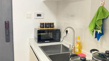 Een moderne keuken met een magnetron, spoelbak, fornuis en een klein schapje met theezakjes, suiker en koffie.