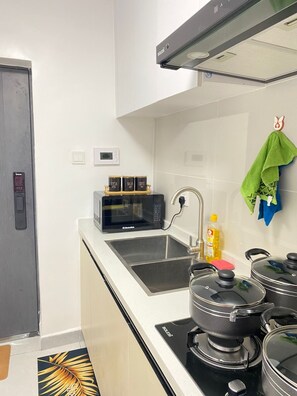 A modern kitchen with a microwave, sink, stove, and a small shelf with tea, sugar, and coffee containers.
