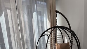 A room with a hanging chair, sheer curtains, and a tiled floor.
