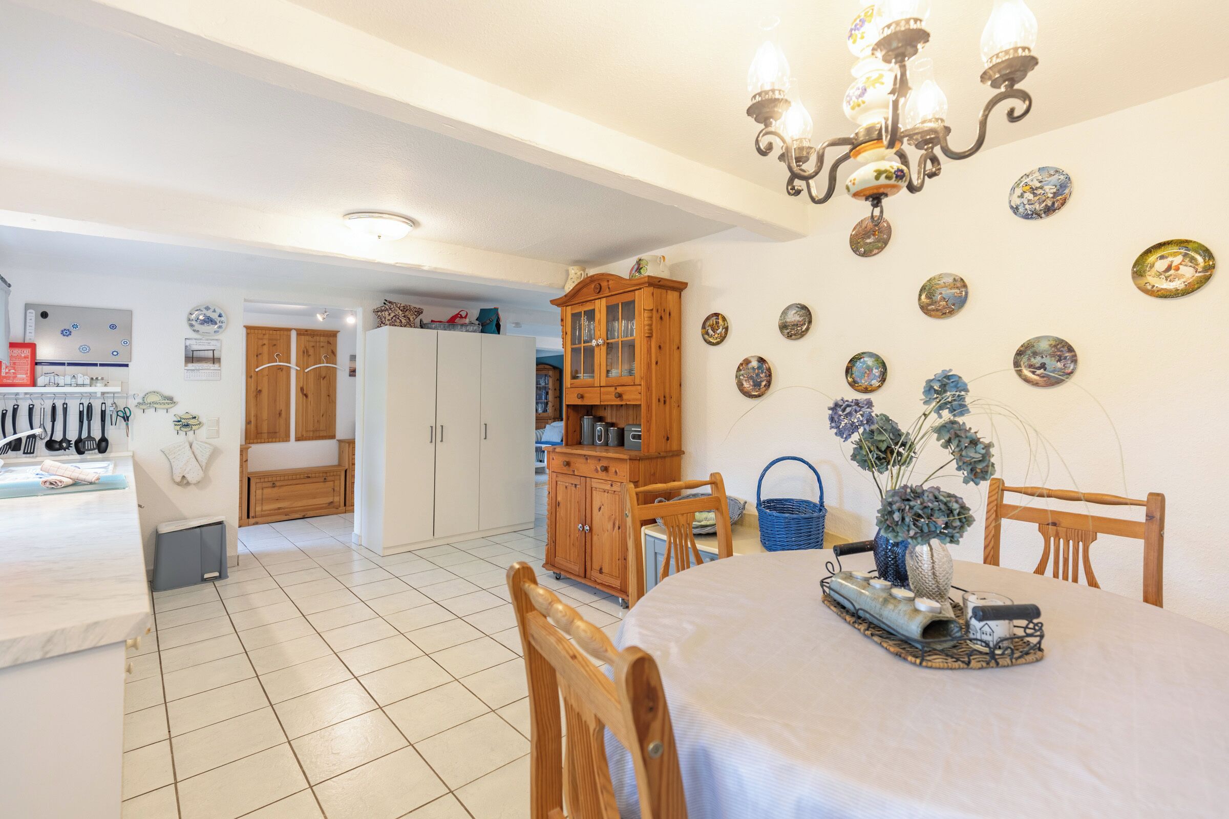 Ein Essbereich mit rundem Tisch, Holzstühlen, einer Chandelüster und an der Wand befestigten Tellern.