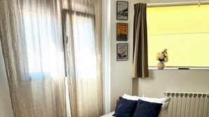 A neatly made bed with a checkered bedspread, a bedside table with a lamp, and a window with curtains. - La Arquita, tu apartamento en Valladolid (Valladolid)