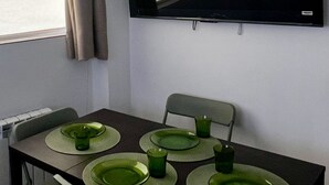 Spiseområde med et bord dækket til fire personer, et fladskærms-tv på væggen og et vindue med gardiner.